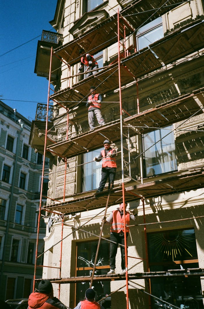 services-05 Construction workers on scaffolding renovating a building facade on a sunny day.